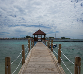 A wooden bridge leading to gazebo with villager house in the background at Harapan Island, Indonesia