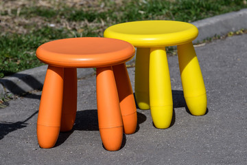 Two little colourful plastic rounded chairs for children on asphalt in a park, yellow and orange bright colours