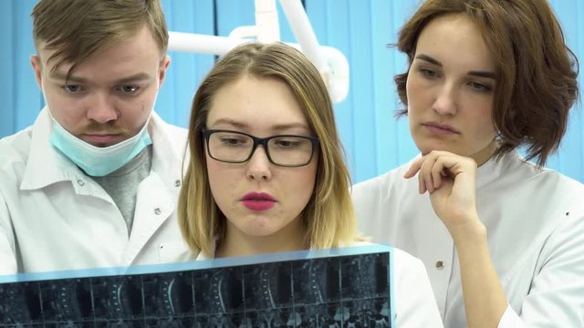 Three young doctors looking at full body x-ray radiographic image, ct scan, mri on hospital clinic cabinet background. Dentists in white lab coats standing and discussing diagnosis.