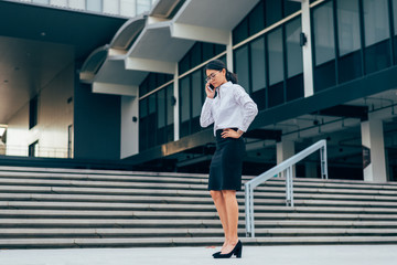 Asian businesswoman in eyeglasses using smartphone talking business discussion with feeling stressful- worry and anxiety standing in front office building- woman officer worker- businesswoman concept