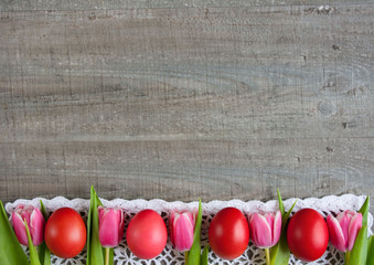 Różowe i czerwone pisanki i różowe tulipany na białej koronce na tle szarych desek