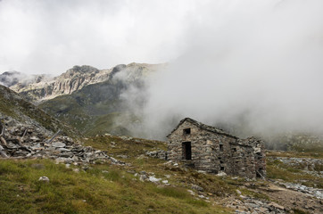 Ruin of old refuge in clouds. Monte Rosa massif near Punta Indren. Alagna Valsesia area, Italy