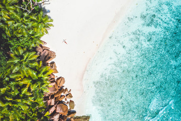 Aerial photo of exotic tropical white sand beach with young woman sunbathing relaxing. Concept of travel vacation holidays in paradise