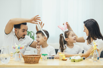Inspired family involved in Easter atmosphere. Mother and father readjusting pink bunny ears on...
