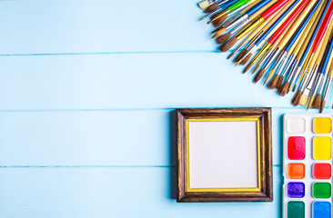 Paints, brushes and palette on the blue wood background. The workplace of the artist. Banner for...