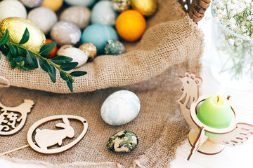 Happy Easter. Stylish Easter candle, eggs, easter bread cake, ham, beets, sausage, butter, green branches in wicker basket on white wooden background with  decorations