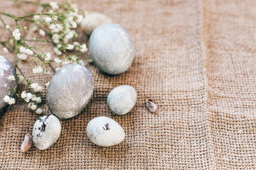 Obraz na płótnie Canvas Stylish Easter eggs with spring flowers on rustic fabric in sunny light on wood. Modern colorful eggs painted with natural dye in grey marble. Happy Easter, greeting card