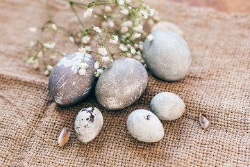 Stylish Easter eggs with spring flowers on rustic fabric in sunny light on wood. Modern colorful eggs painted with natural dye in grey marble. Happy Easter, greeting card