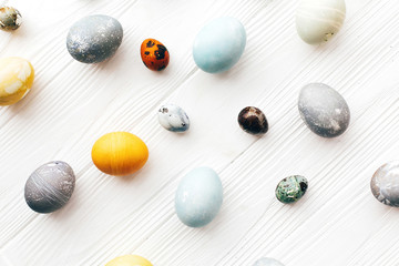 Happy Easter greeting card. Stylish Easter eggs flat lay on white wooden background. Modern easter eggs painted with natural dye in yellow,blue,green,grey colors. Creative pattern