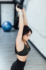 young brunette model in black sportswear exercising with dumbbells.
