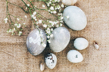 Obraz na płótnie Canvas Stylish Easter eggs with spring flowers on rustic fabric in sunny light on wood. Modern colorful eggs painted with natural dye in grey marble. Happy Easter, greeting card. Top view
