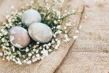 Fototapeta na wymiar Happy Easter, greeting card. Stylish Easter eggs with spring flowers in floral nest on rustic fabric in sunny light on wood. Modern colorful eggs painted with natural dye in grey marble