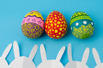 Colorful decorated eggs and white bunny paper chain on blue background. Easter Day decoration