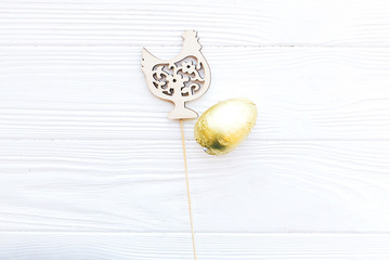Stylish Easter chocolate egg in golden foil and simple wooden chicken decoration on white wooden...