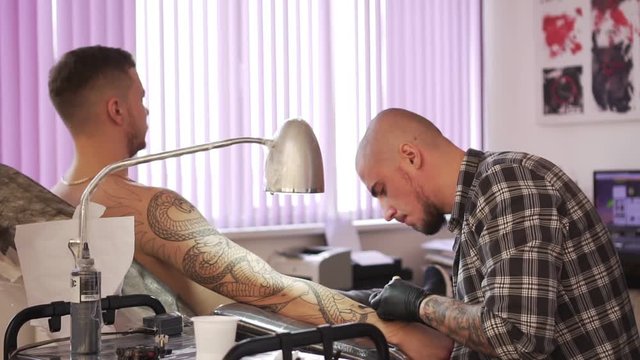 A man makes a tattoo on his arm in a tattoo studio, slow motion.