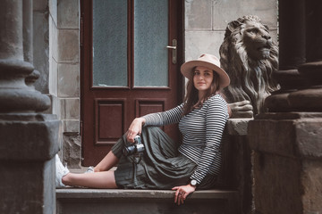 Beautiful woman in a striped shirt and hat. Holds the camera near the statue of a lion against the background of the old house