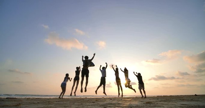 Silhouette of friends jumping on beach during sunset time with happy emotion. 4K resolution. Slow motion shot.
