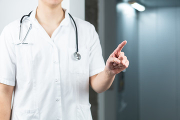 Bright close up of male doctor in uniform with stethoscope pointing finger in the air. Copy space...