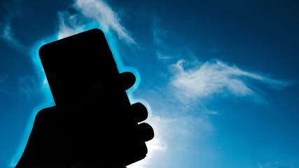 Human hand holding smartphone over blue sky background,phone radiation concept