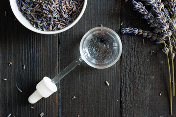 lavender perfume product sample at pipette and flowers on black wooden table background