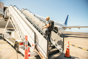 Naklejka premium A Young traveling man get in the plane with passport on the landing strip