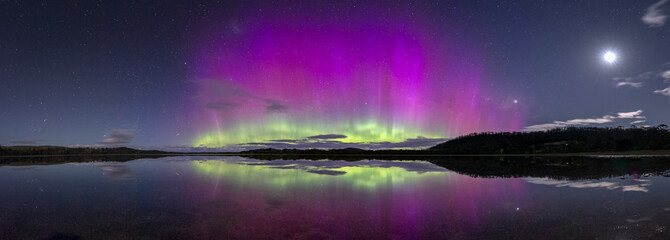 A spectacularly bright and colourful display of the Aurora Australis or Southern Lights with reflection in water - obrazy, fototapety, plakaty