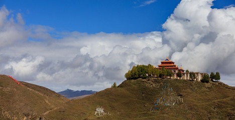 Buddhist Temple on the top of a hill, Tibetan Village of Bamei situated in the grasslands of Sichuan Province, China. blue sky white clouds in the distant background. Tagong and Xinduqiao scenery