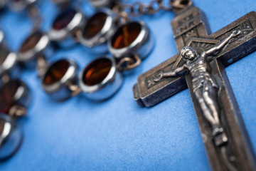 An extreme close-up or macro shot with selective focus of a rosary with glass beads encased in metal pods set on a plain blue background.