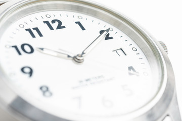 A macro shot with selective focus of the white dial of a round watch face with big numbers.