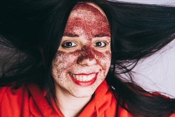 Crazy girl posing in a red hoodie with a painted face. Bizarre portrait with painted face