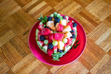 Beautiful Fruit Salad in a Watermelon Bowl Plated on a Red Dish on a Parquet Wood Table