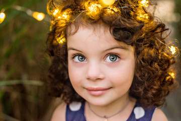 A beautiful little girl with big eyes and dark curly hair gently cares for her goldfish. Festive lights in her hair.