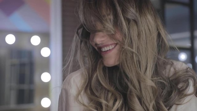 beautiful young girl with long curly hair flaunts and shows off in front of a mirror, flirts, flirts, smiles, sultry look, happy, pleased with herself, beautiful makeup, sexy lips