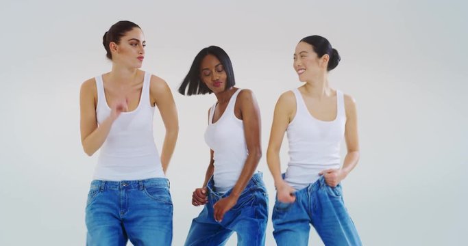 Slow motion of beautiful young smiling women of different ethnicities with perfect firm and slim body in white tank shirts dancing, having fun and showing weight loss by wearing old jeans. 