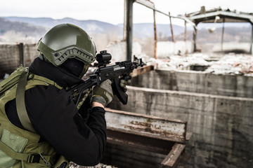 Young Special forces SWAT soldier aiming with assault rifle gun at the ruined building war...