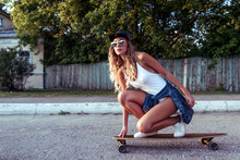 Tanned woman, fashionable and stylish girl rides on the way to the skateboard, longboard. White bodysuit swimsuit, sunglasses baseball cap. In the summer in the city has a rest. Free space for text.
