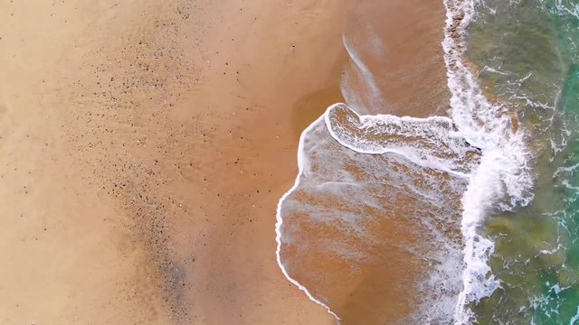 4k UHD aerial view of waves motion over multicolored sandy sea coast
