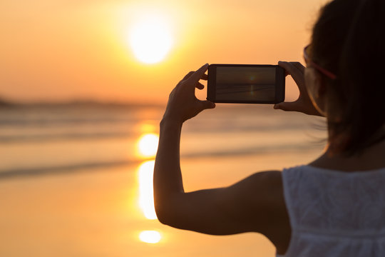 Young woman taking picture of sea sunset
