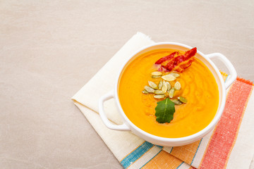 Pumpkin cream soup. White ceramic bowl with fresh pumpkin, dry seeds, smoked bacon. With vintage linen cloth (napkin) on stone background