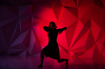 Woman dancing on the background of a beautiful multicolored wall. Sexy slim lonely girl with long black hair in a beautiful dark blue dress. covered her face with her hands. bright colorful geometry
