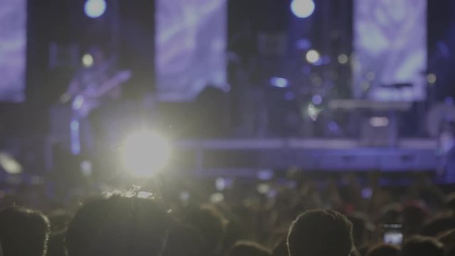 4K Panning shot blurred celebrate blurred rock music star singer in concert with blinker and spotlight background on stage. Hands of people enjoying concert waving and take a photo smartphone.