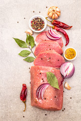 Raw pork tenderloin with vegetables and spices. Cooking meat background, fresh brisket boneless steak on stone background, top view, close up.