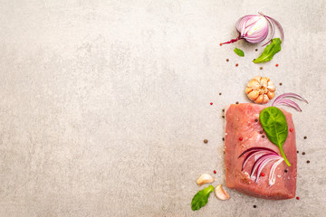 Raw pork tenderloin with vegetables and spices. Cooking meat background, fresh brisket boneless steak on stone background, top view, copy space.