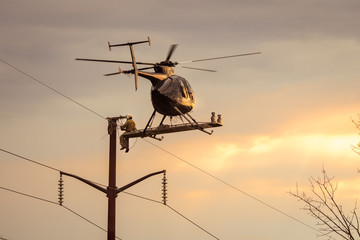 Helicopter hovering in flight with man sitting on the outside fixing power lines repairing wires © Pete
