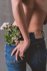 Fashion background, a woman with no shirt is wearing a blue jeans  and turning her back to the camera. In the back pocket of her jeans has many flowers sticking inside.