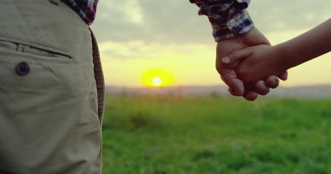 Close up of the Caucasian hand in hand of grandfather and granddaughter in the middle of the field on the sunset.