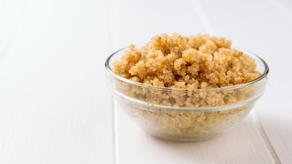 Glass bowl with boiled quinoa on a white wooden table. A gluten-free boiled cereal dish.