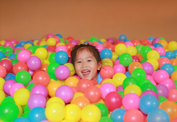 Fototapeta na wymiar Happy little Asian child girl playing with colorful plastic balls playground.