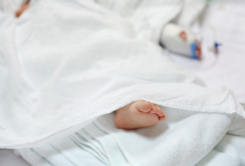 Close up patient baby feet sleep on bed at hospital with blur Saline intravenous drip on baby&rsquo;s hand.
