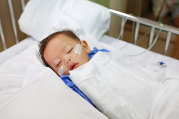 Baby boy age about 1 year old sleeping on patient bed with getting oxygen via nasal prongs to...